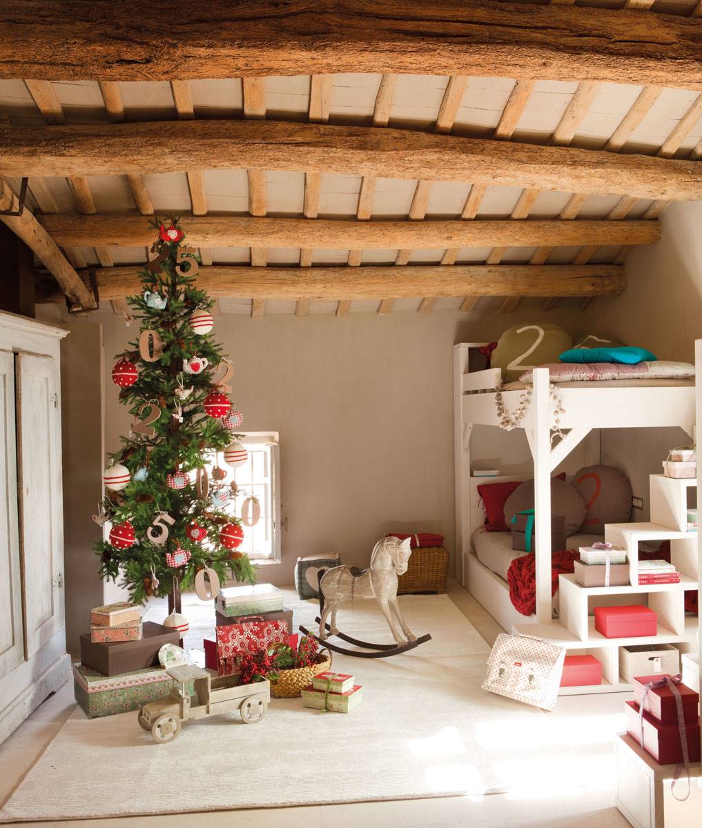 Dormitorio infantil con vigas en el techo, literas y árbol de Navidad estrecho decorado con adornos rojos. 