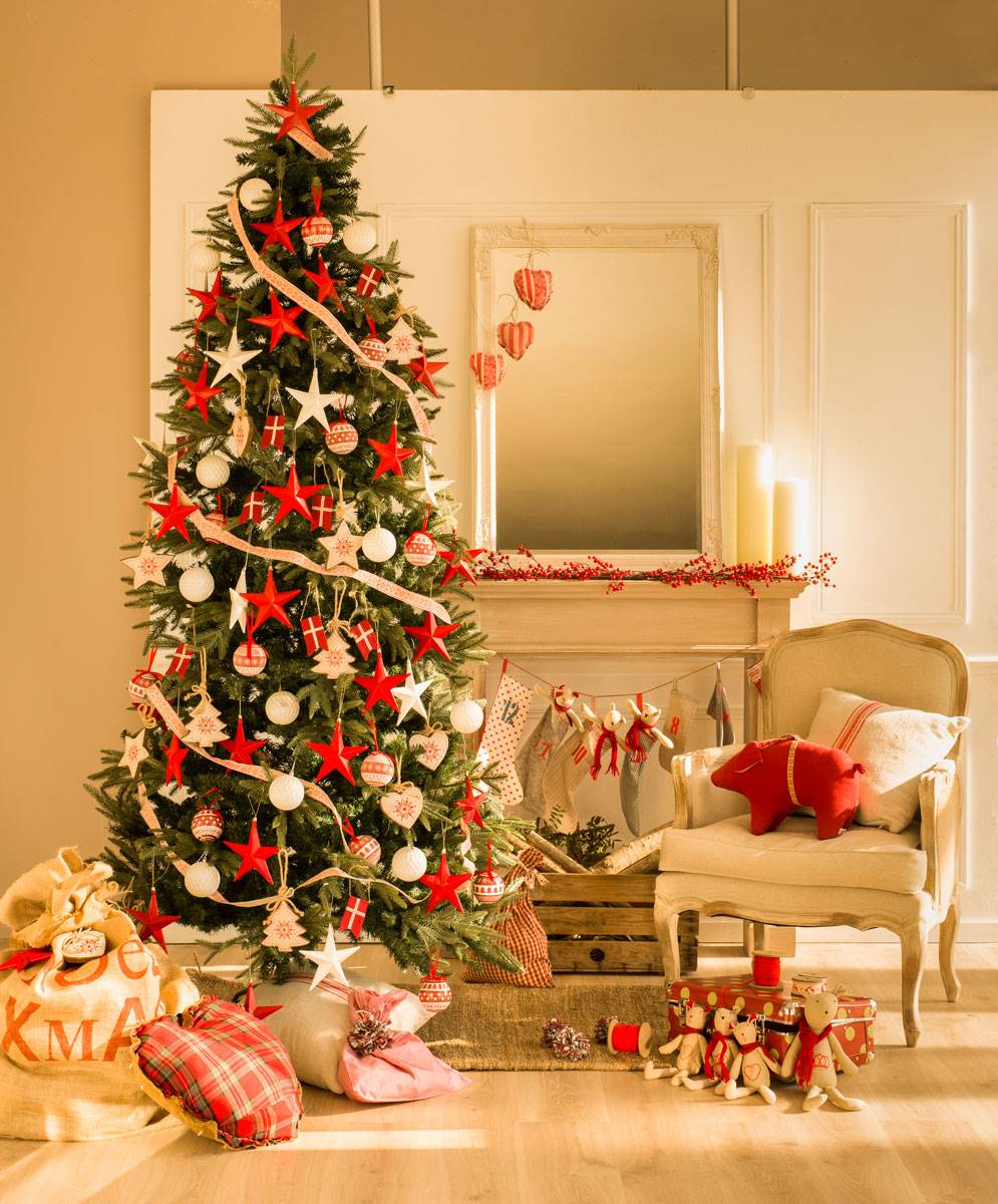 Salón con árbol de Navidad tradicional decorado en blanco y rojo junto. ala chimenea y butaca. 