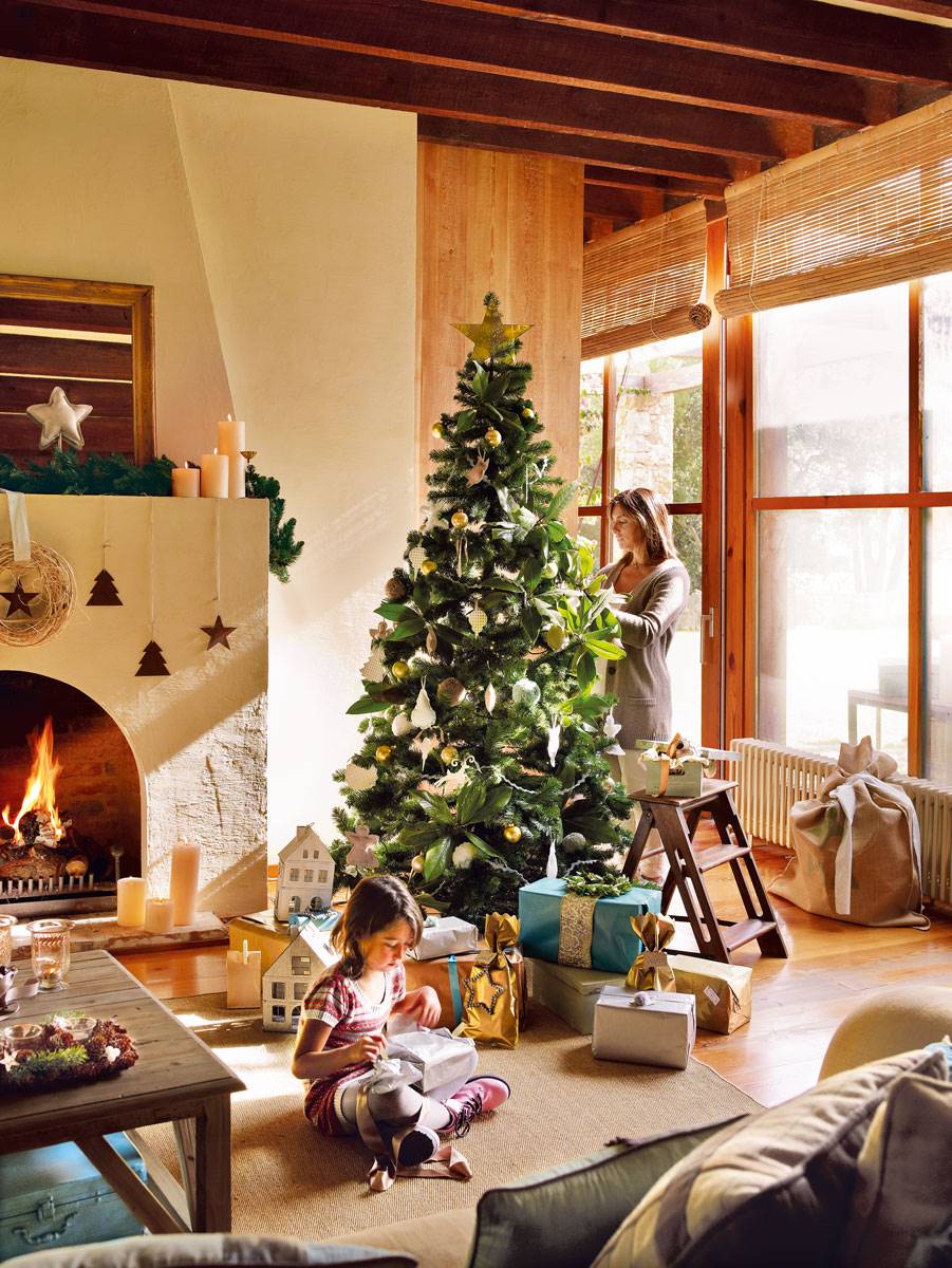 Salón rústico con chimenea, techo de vigas de madera, y árbol de Navidad decorado con hojas de magnolio.