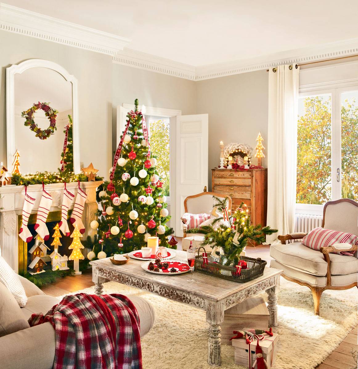 Salón clásico con alfombra, butacas, chimenea y árbol de Navidad con adornos rojos y blancos. 