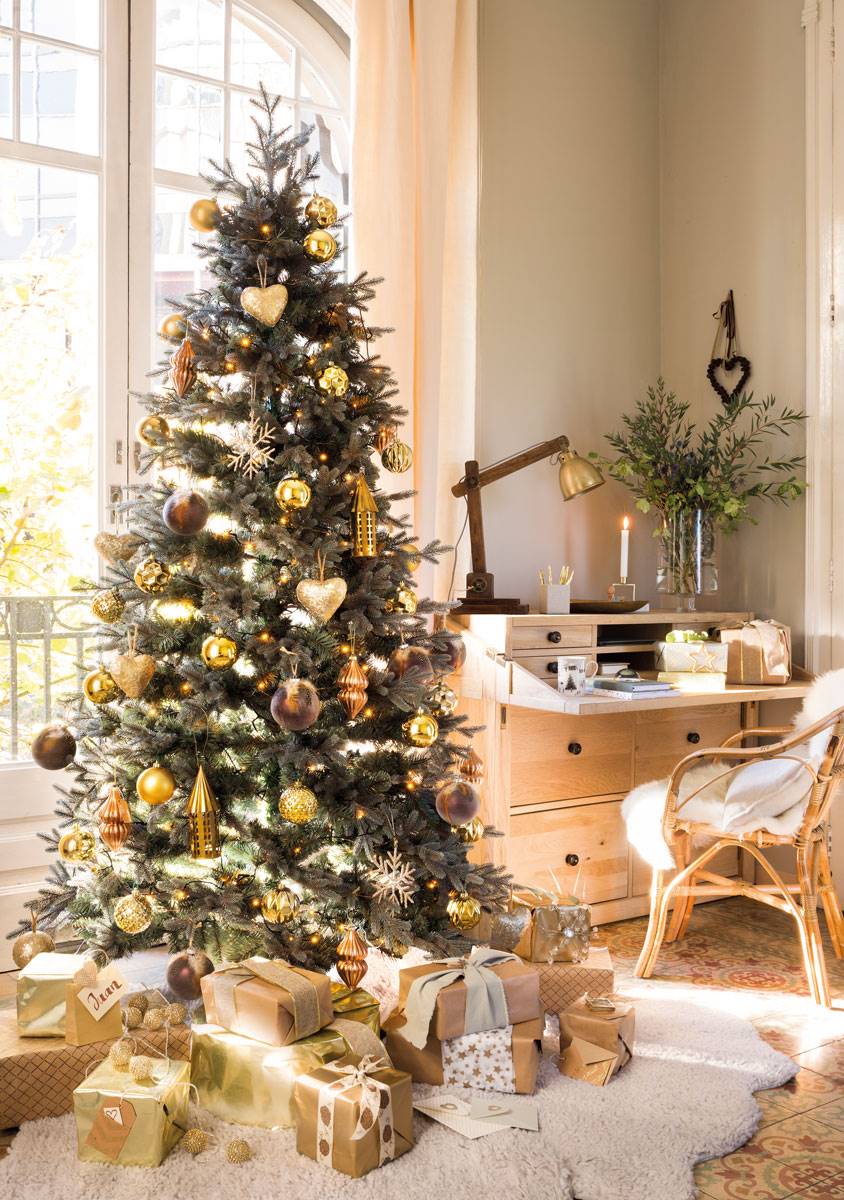 Zona de trabajo con árbol de Navidad cerca decorado con adornos dorados. 