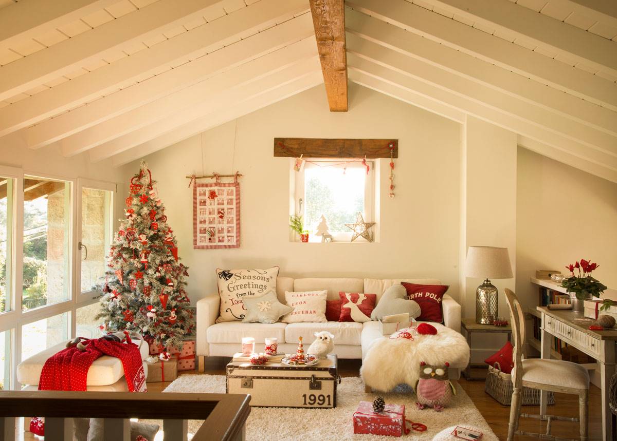 Salón en la buhardilla de color blanco con decoración Navideña en rojo y un árbol de Navidad.