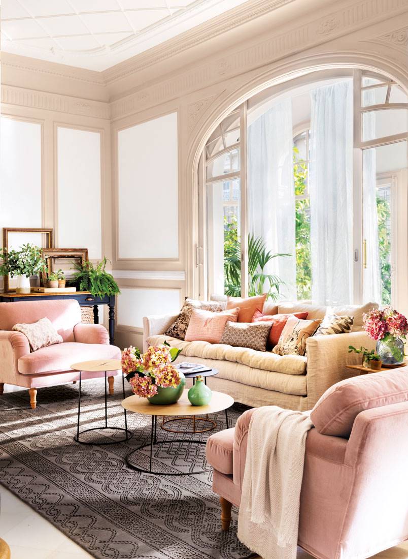Salón regio con gran ventanal y distribución en "U" de sofá y butacas rosas