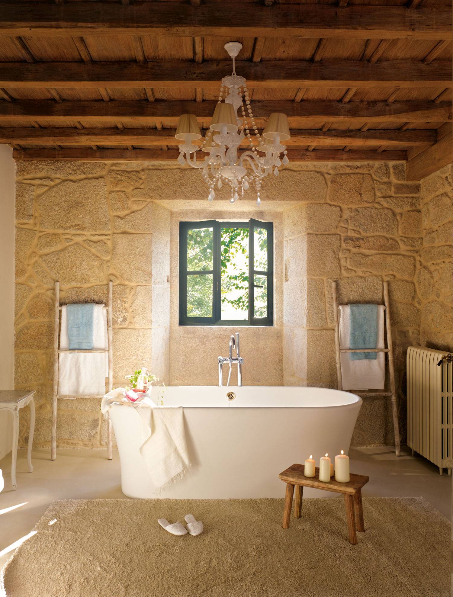 Baño rústico con paredes de piedra, lámpara de araña en el techo y bañera exenta.
