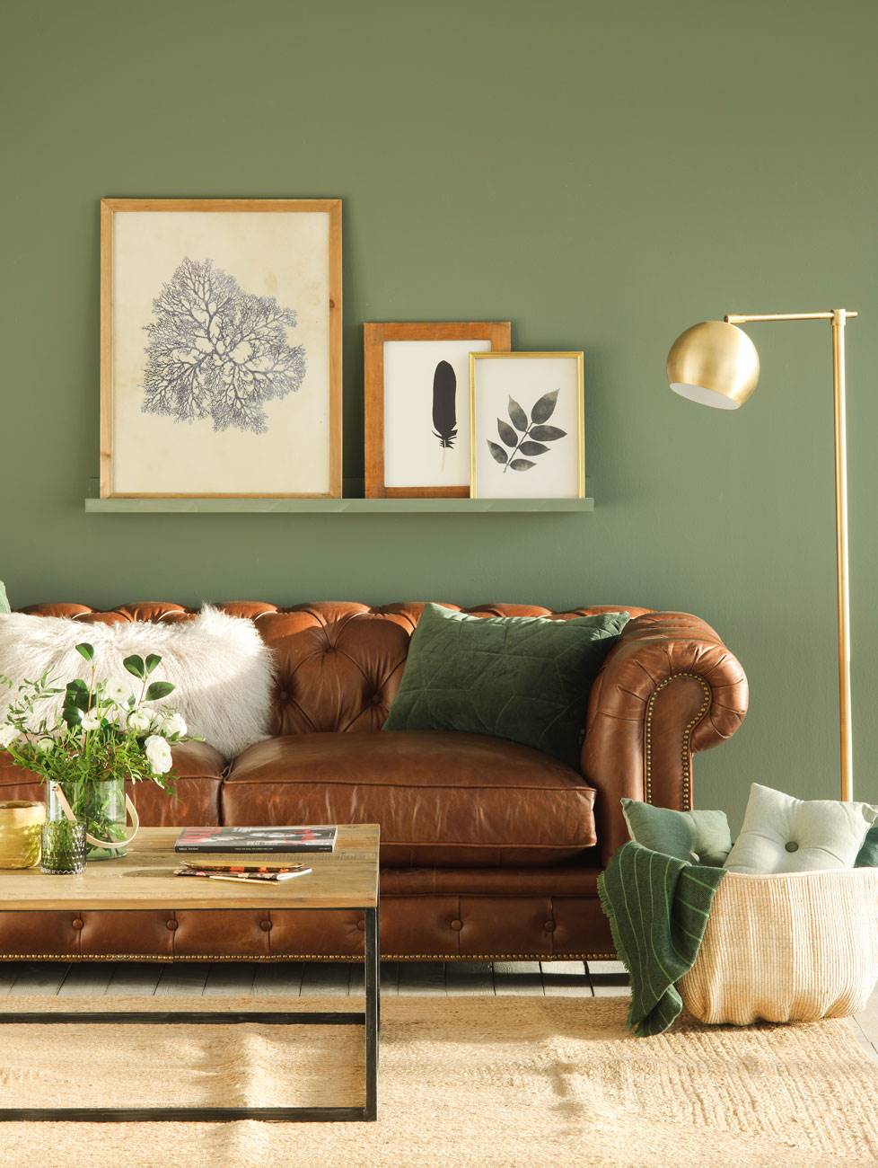 Salón con sofá chéster, cuadros en el estante, alfombra y lámpara de pie dorada.