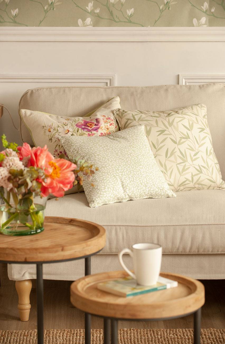 Salón con sofá beige, arrimadero, cojines y mesitas de madera de centro.
