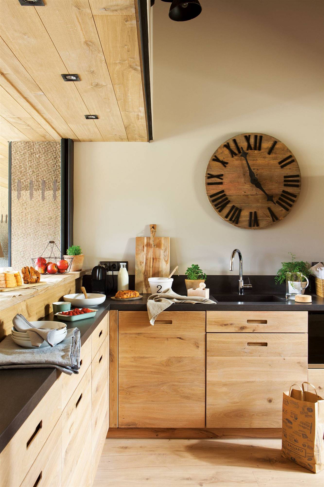 Moderna cocina con mobiliario diseñado a medida en madera, encimera en negro y gran reloj en la pared. 