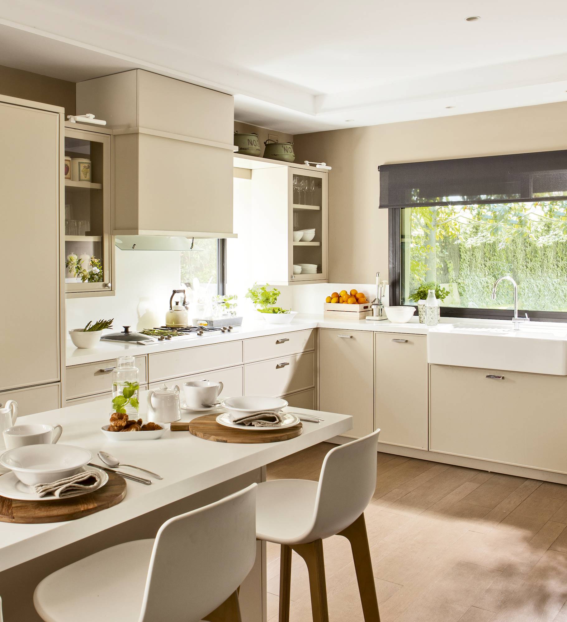 Moderna cocina con mobiliario en color crema, ofice a juego y pavimento de madera. 
