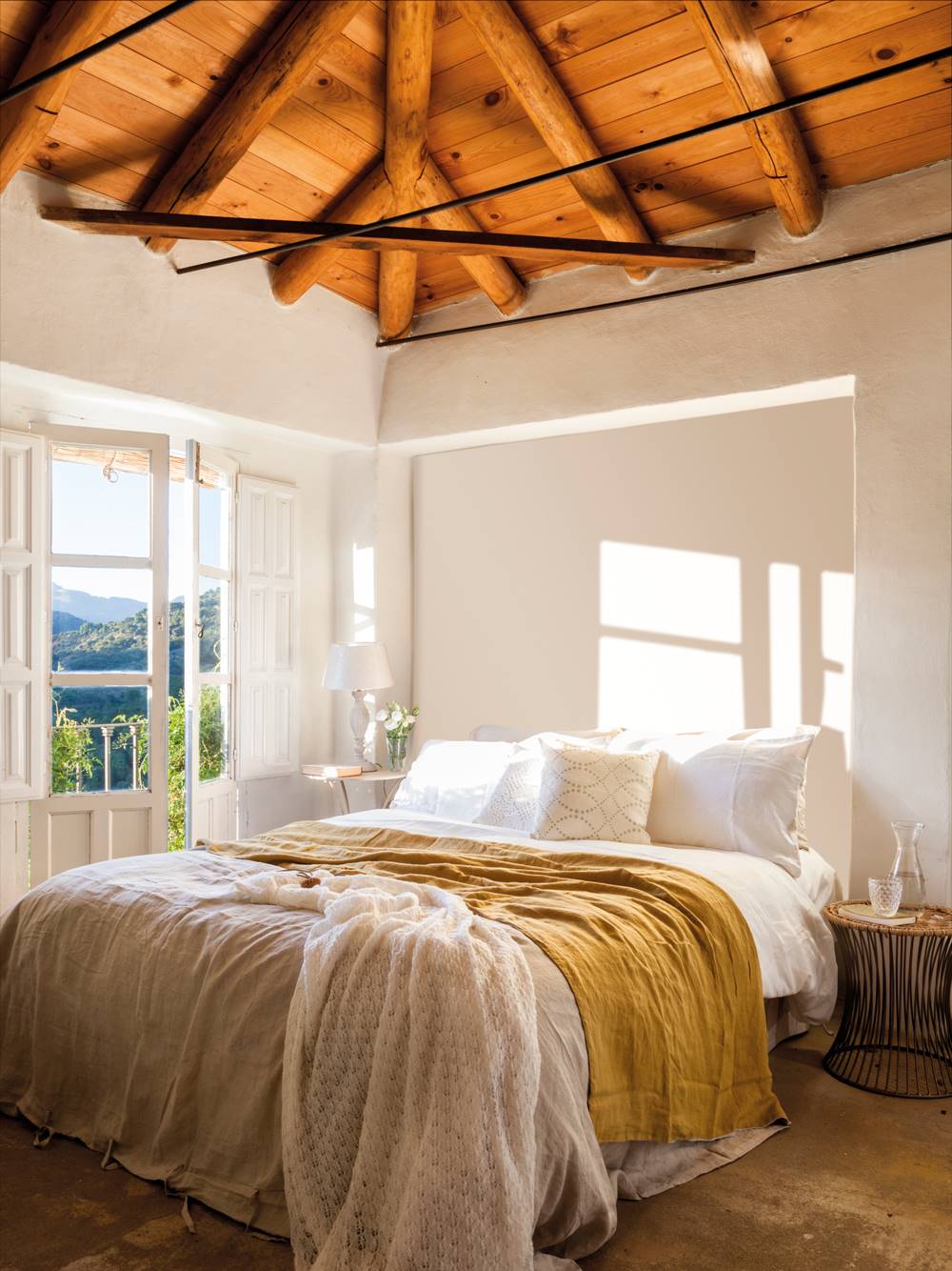 Dormitorio con techo abuhardillado de madera y paredes blancas. 