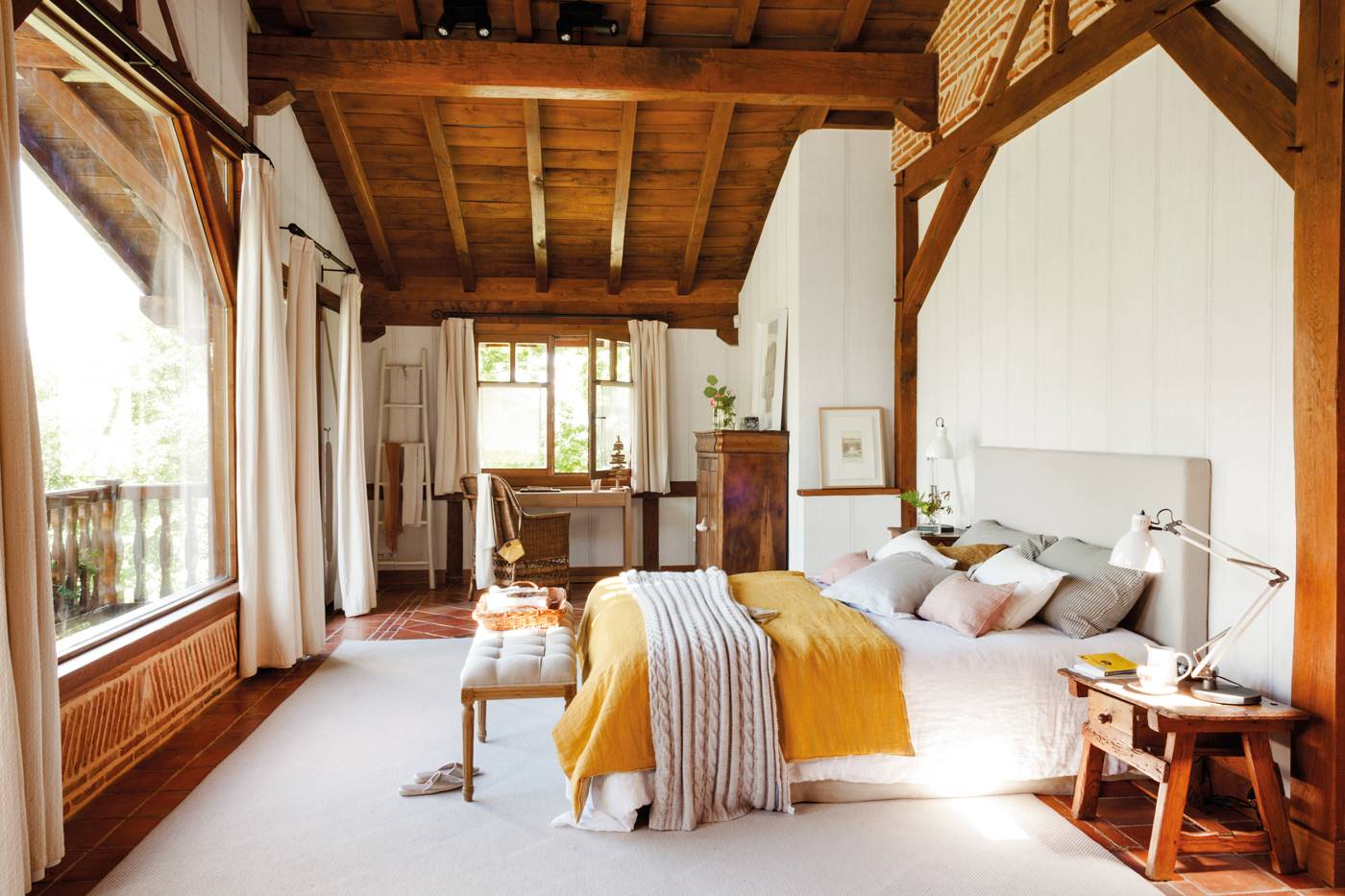 Dormitorio con techos y paredes de madera con ropa de cama blanca y mostaza. 