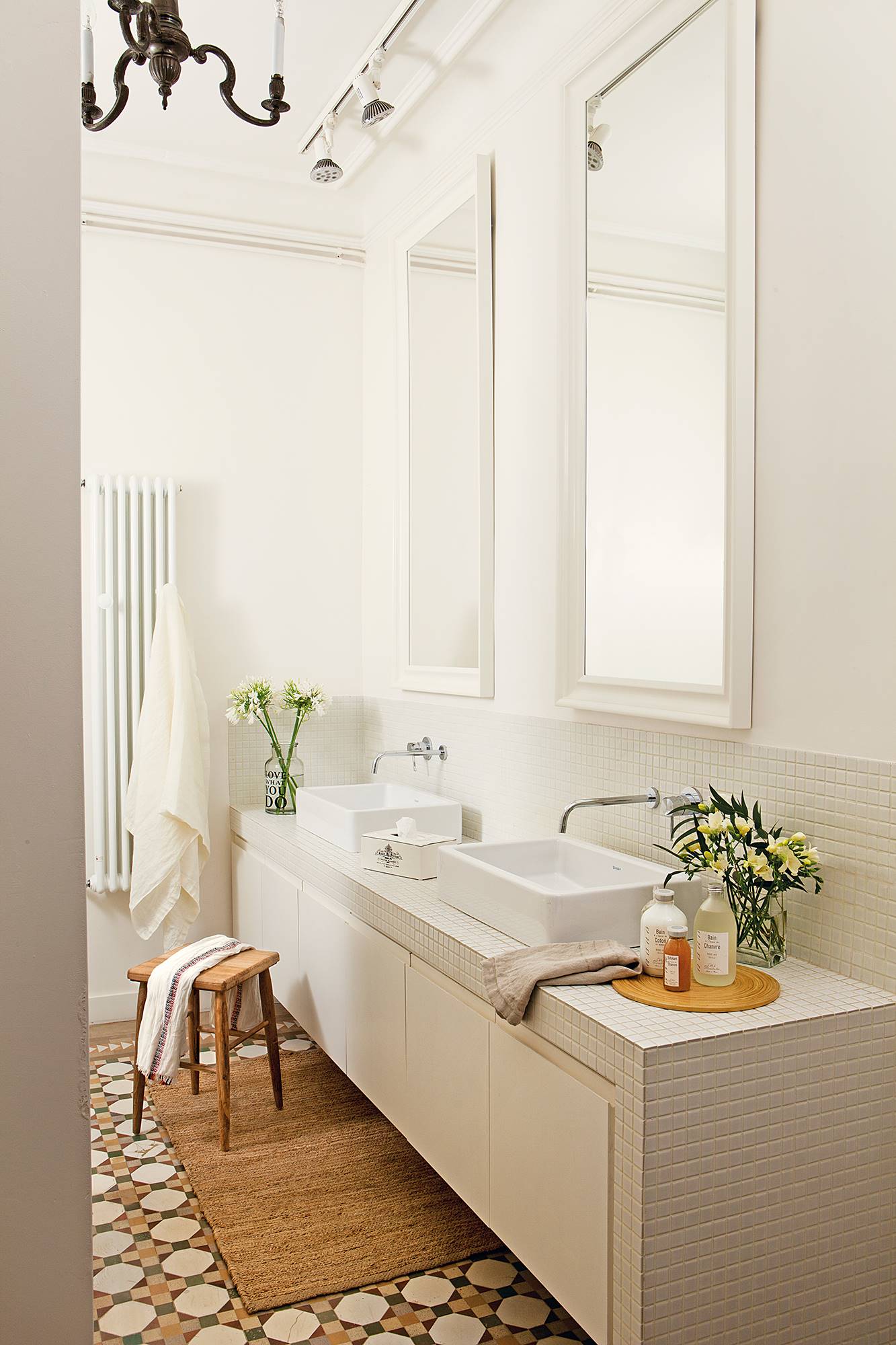 Baño con mueble realizado a medida en blanco, dos espejos, taburete, mosaico en el suelo y radiador para toallas.