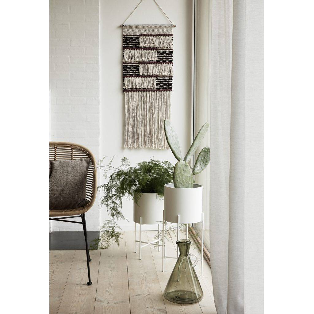 Salón con plantas, maceteros blancos con plantas y pared con tapiz de algodón.