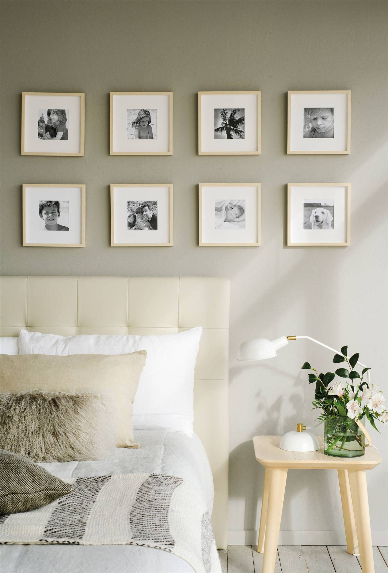 Dormitorio con cabecero blanco de capitoné, mesita auxiliar de madera y composición de cuadros de fotografías en la pared.