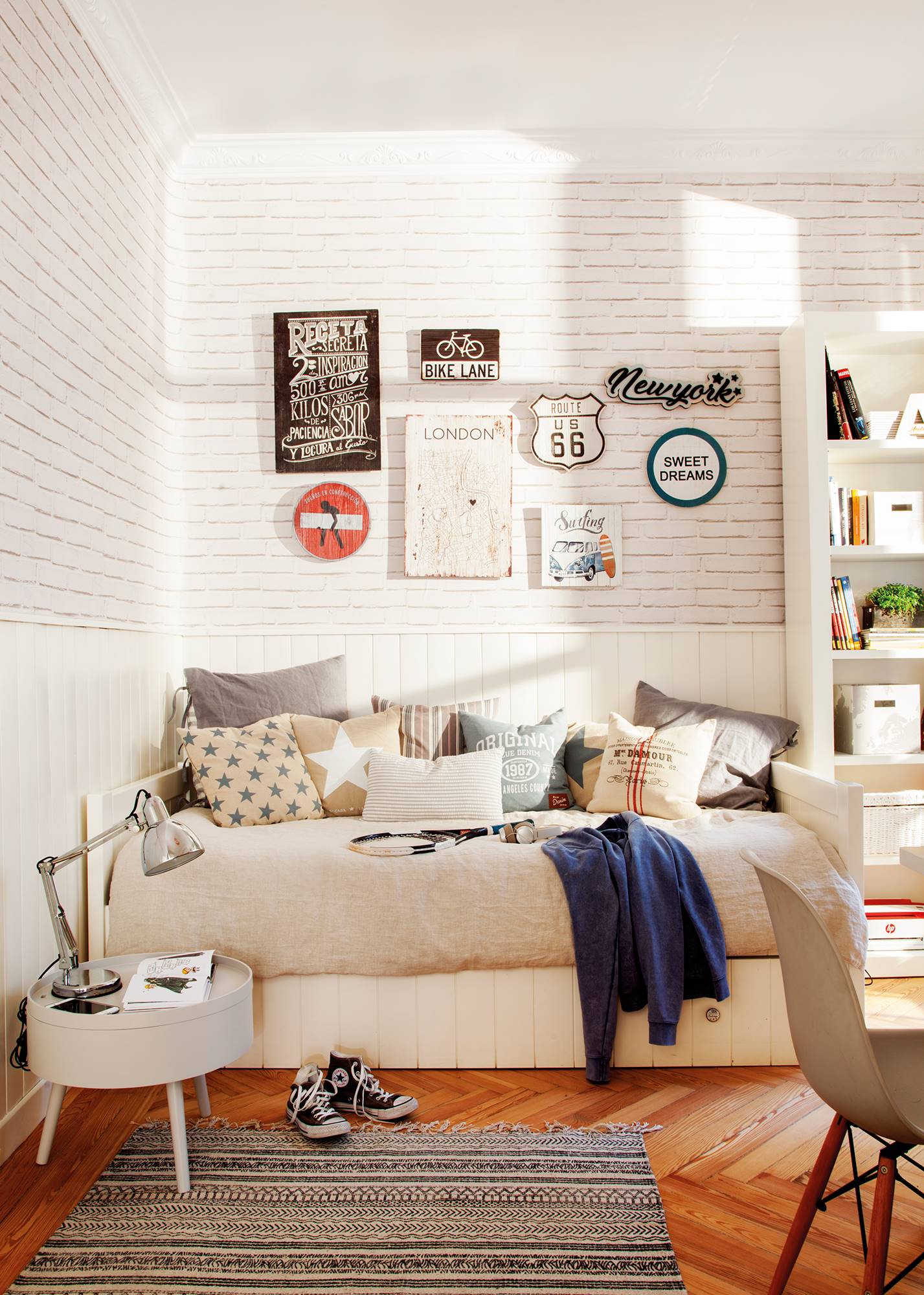 habitación juvenil con cama. enla pared, alfombra, librería, arrimadero blanco y pared con ladrillos con letreros decorativos.