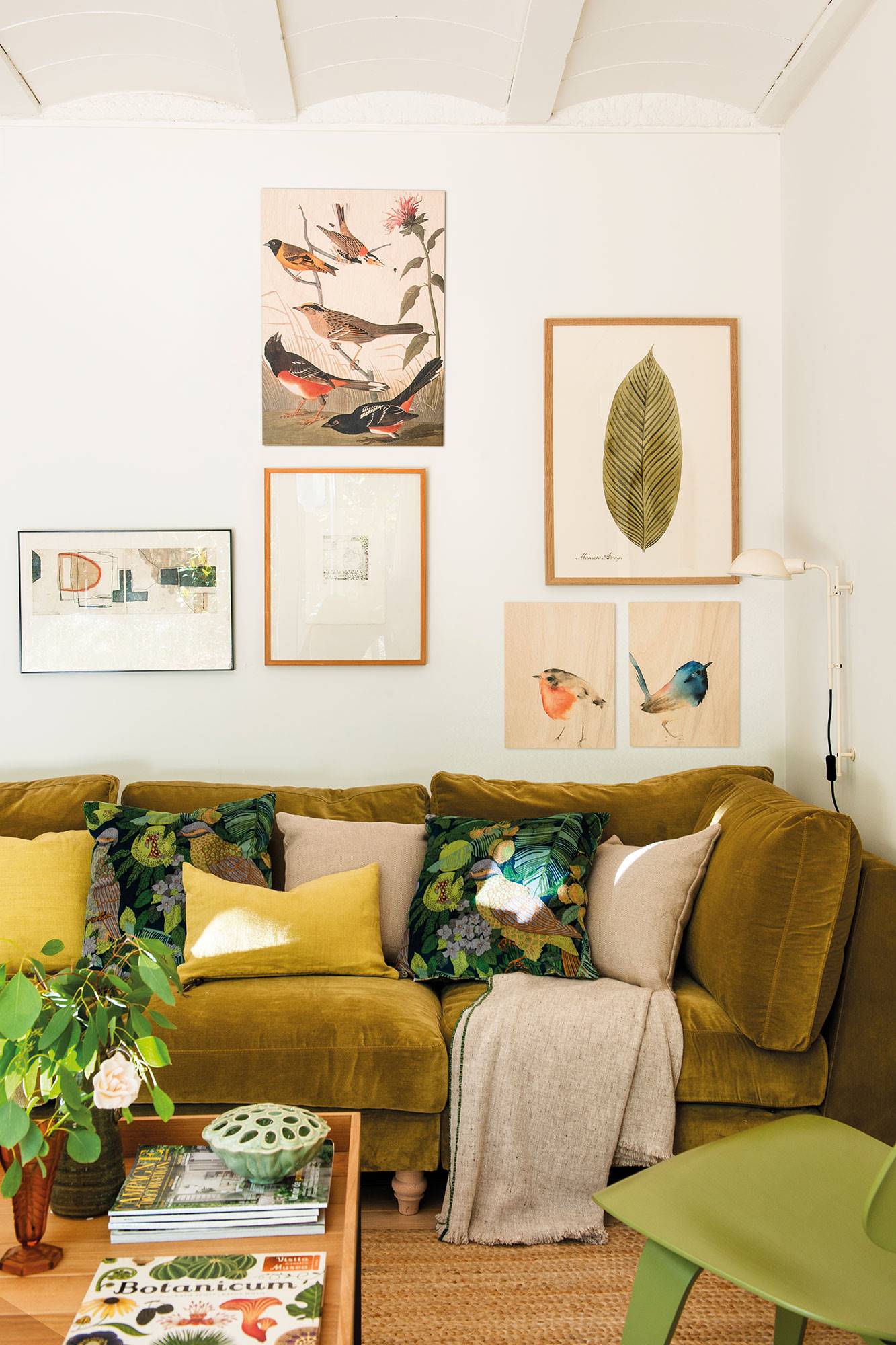 Salón con sofá de terciopelo verde, cojines estampados y amarillos  y láminas decorando la pared.