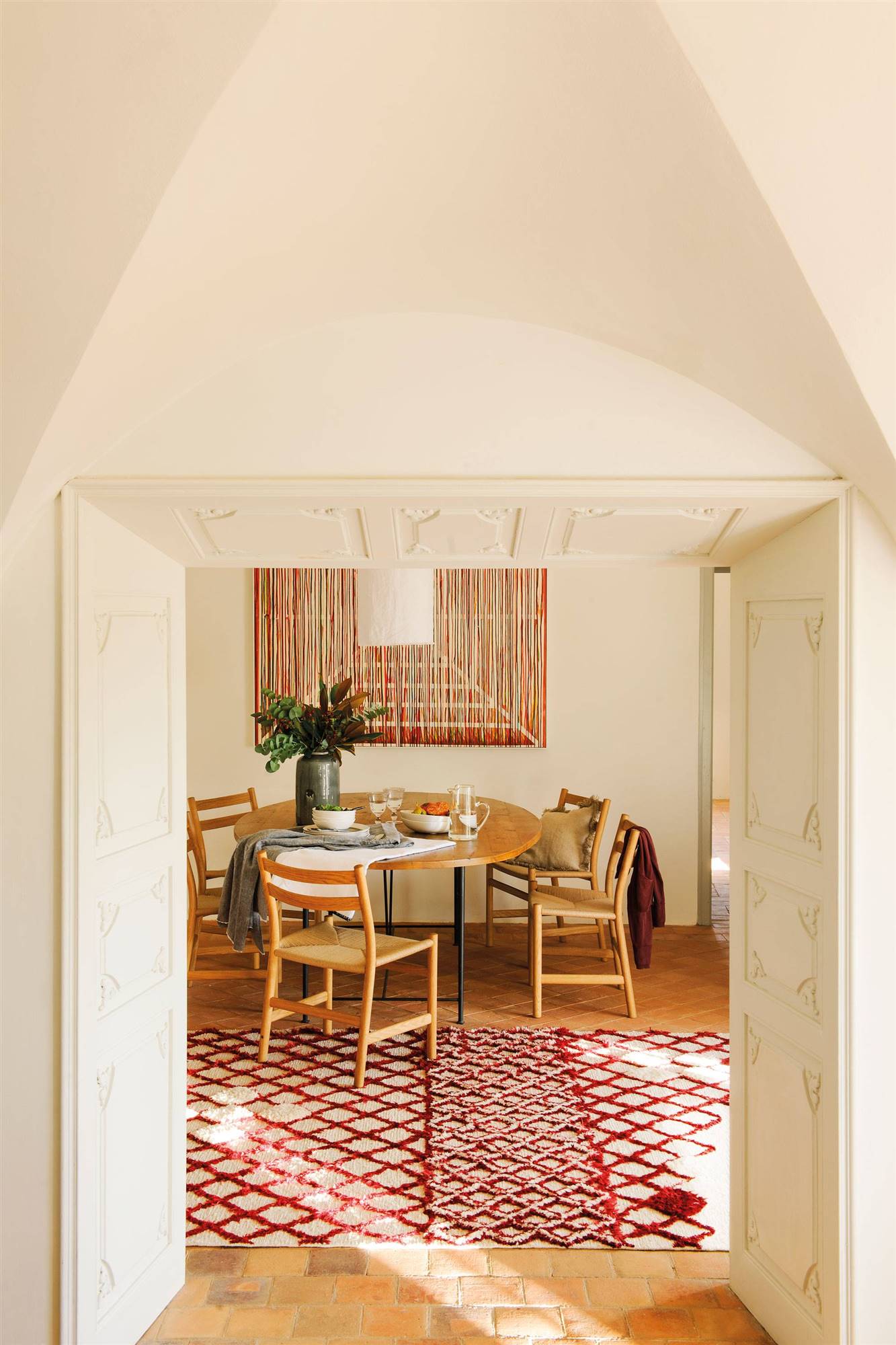 Comedor con mesa de madera, alfombra y pared decorada con paneles ornamentados y cuadro.