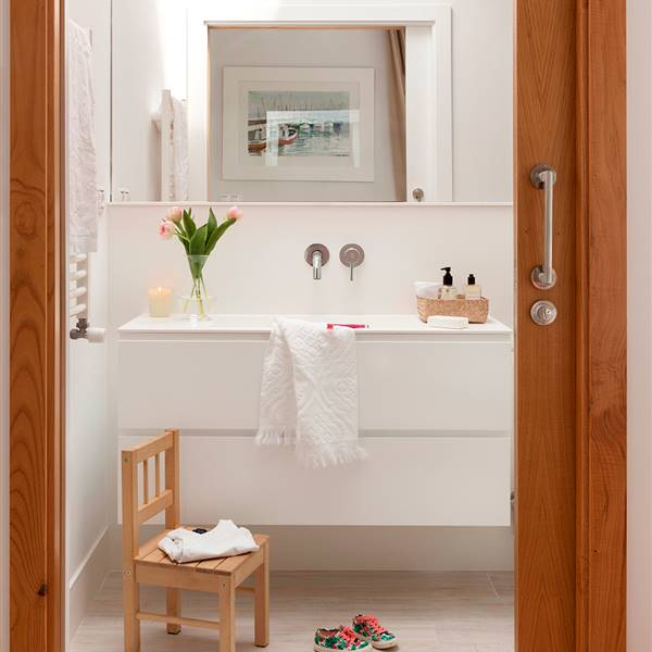 Baño con bajolavabo volado en blanco sin tiradores, espejo, silla de niño y puerta corredera de madera