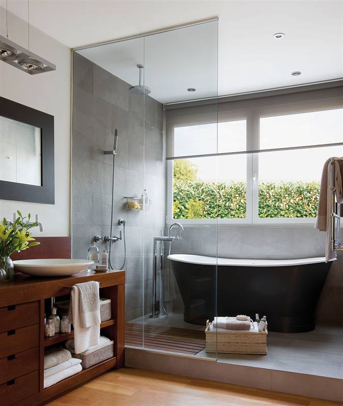 Baño con ducha y bañera exenta separados del resto del baño por mámpara de cristal