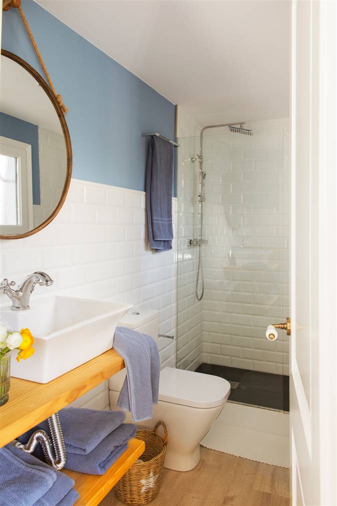 Baño con ducha y mampara, azulejos blancos combinados con pintura azul y espejo redondo 00427819