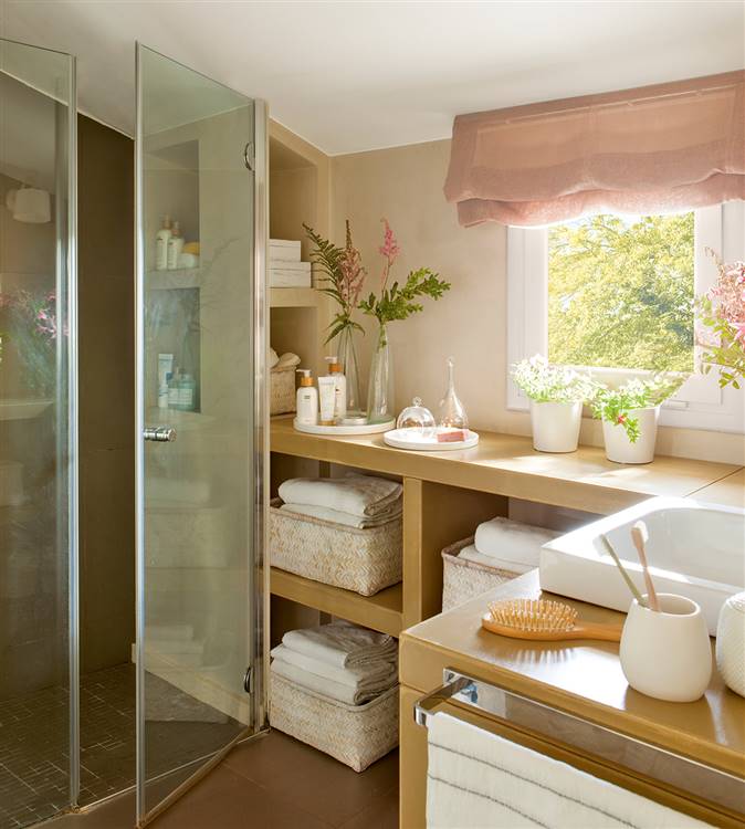 Baño con mueble a medida en forma de L con estantes abiertos, mampara de cristal, ventana y cestas con toallas