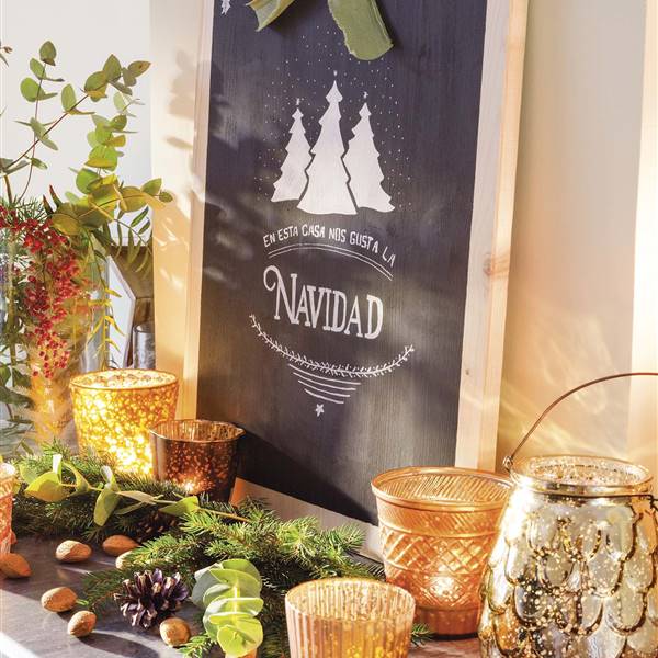 Cartel de Navidad hecho con madera y pintura de pizarra sobre estante de chimenea con velas, ramas de abeto y portavelas