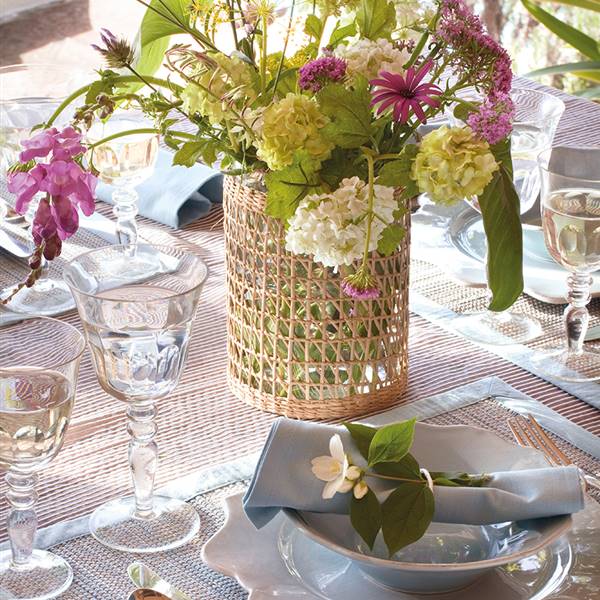 Detalle de mesa con vajilla y jarrón de mimbre con flores