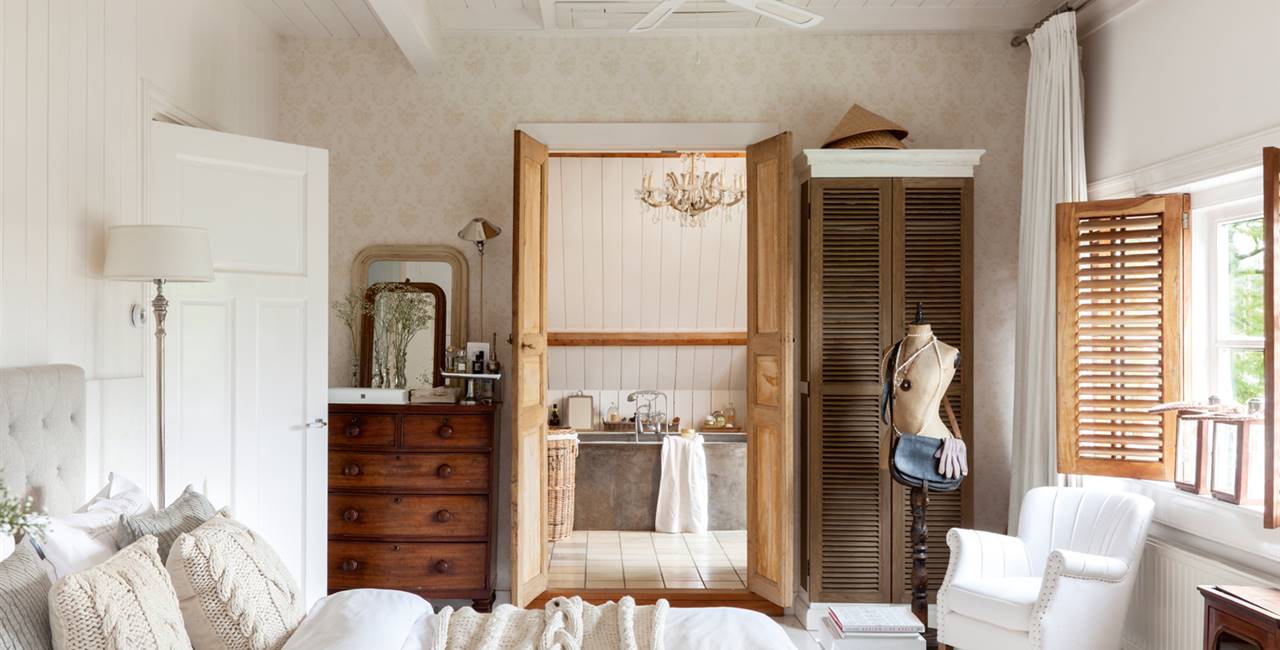 Dormitorio con baño en suite, cómoda antigua, butaca y ropa de cama de lana D00409028