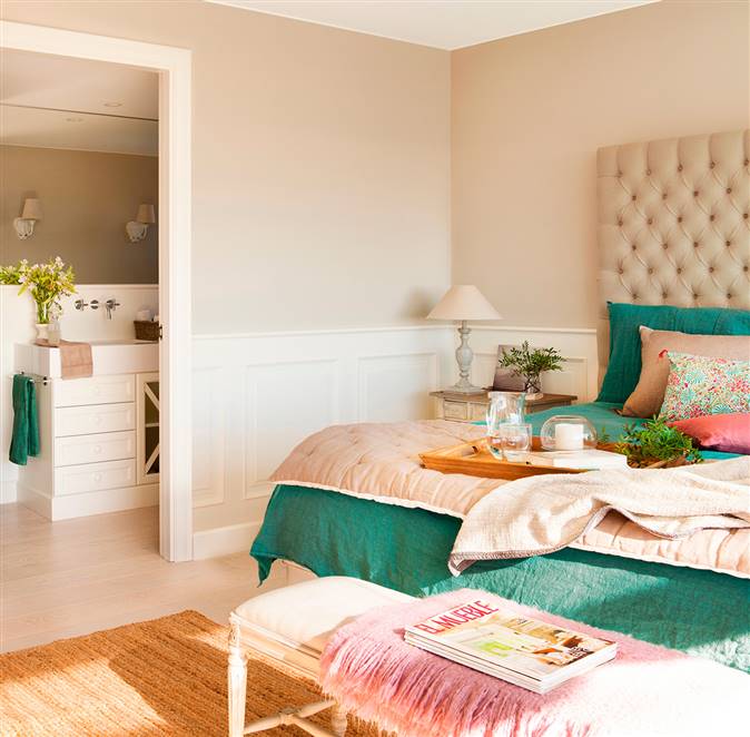 Dormitorio con cabecero en capitoné, ropa de cama verde y rosa, banqueta, arrimadero con molduras y baño en suite