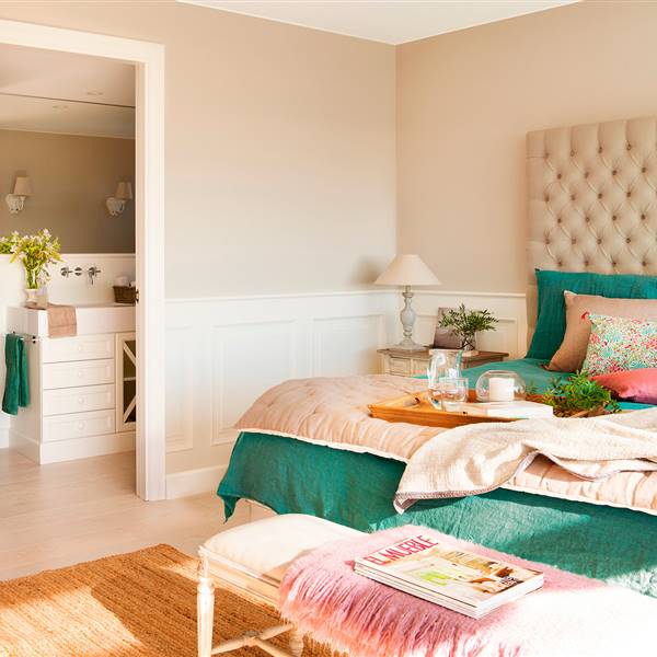 Dormitorio con cabecero en capitoné, ropa de cama verde y rosa, banqueta, arrimadero con molduras y baño en suite