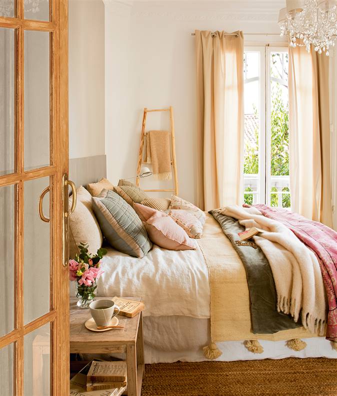 Dormitorio con escalera para colocar manta, cama muy vestida y lámpara de araña