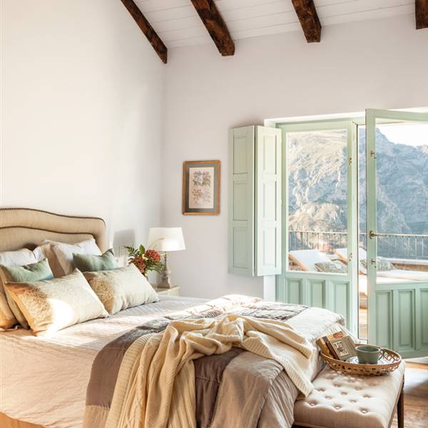 Dormitorio con techo de vigas, ventanal con porticones verdeagua, cama con mantas, banqueta, bandeja y cojines_449892