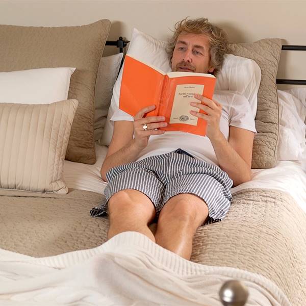Lorenzo Meazza, responsable de interiorismo de Ikea España tumbado en la cama de su dormitorio leyendo
