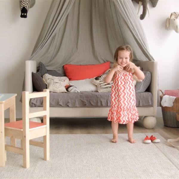 Niña en cuarto infantil de estilo nórdico con muebles de madera clara y gris, alfombra beige y mesita con sillas