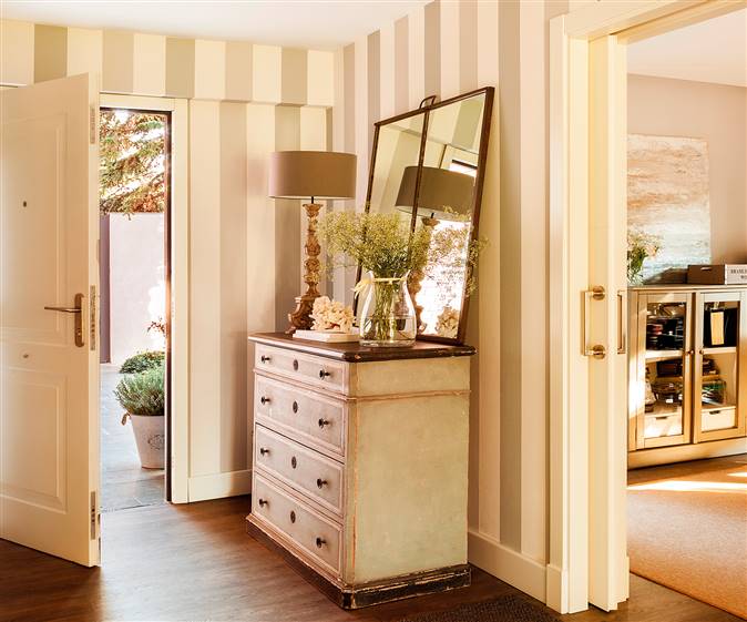 Recibidor con cómoda de madera y espejo conectado con el salón a través de una puerta corredera.