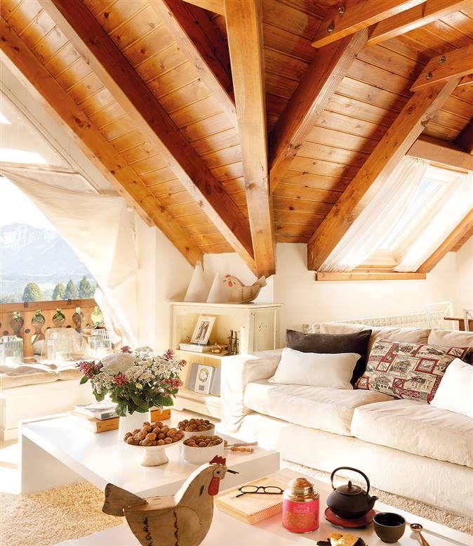 Salón abuhardillado de madera con tapicerías y muebles en tonos blancos