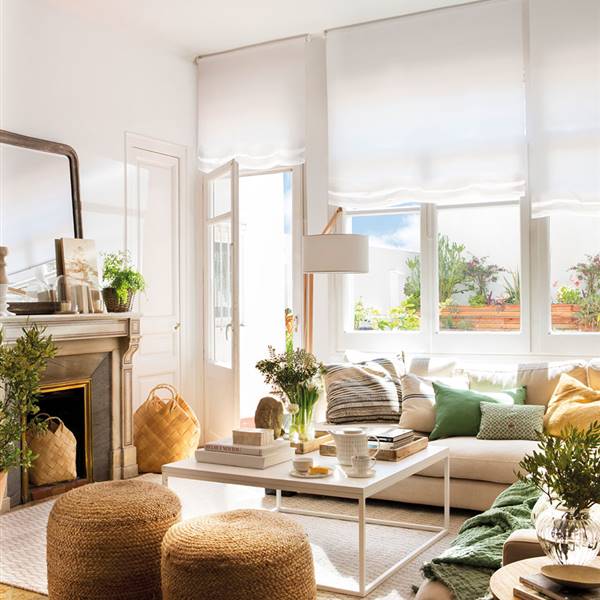 Salón con chimenea y mesa de centro cuadrada encima de alfombra con sofás blancos y pufs de fibras naturales