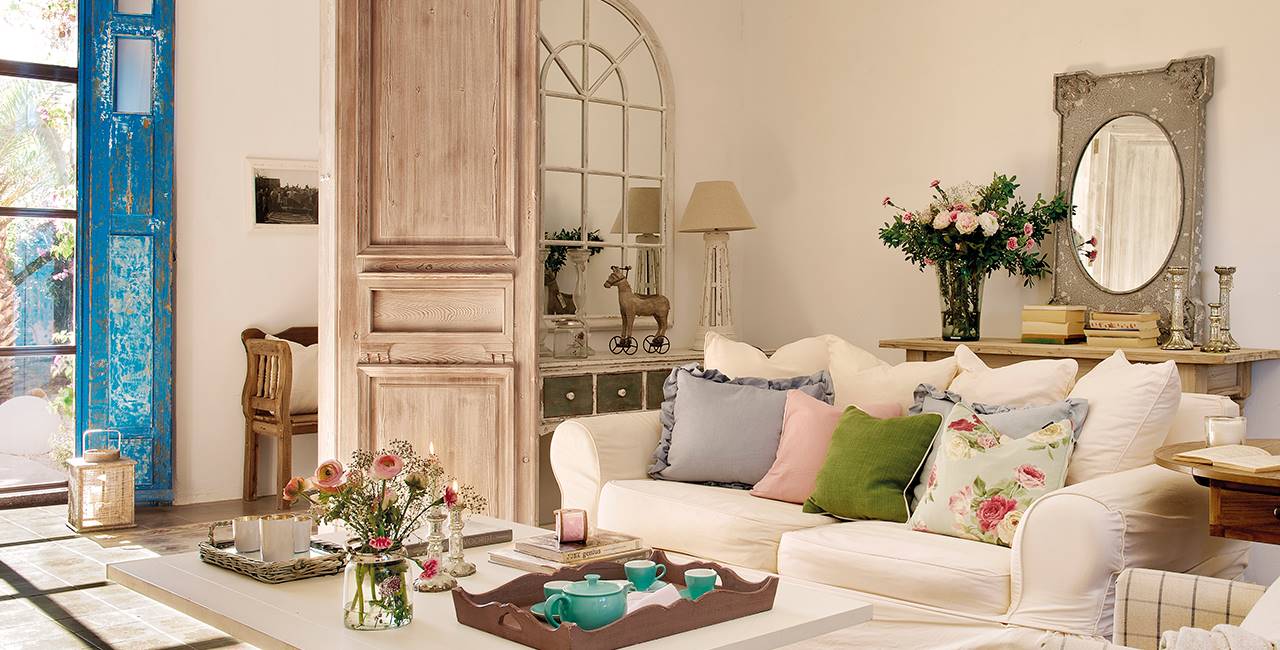 Salón con sofá blanco con cojines primaverales y consola con espejo de cuarterones