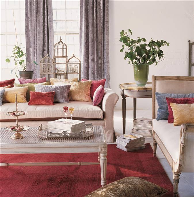Salón decorado con cojines en terciopelo rojo y gris, una mesa de centro blanca, una mesa auxiliar Luis XVI y una alfombra roja.