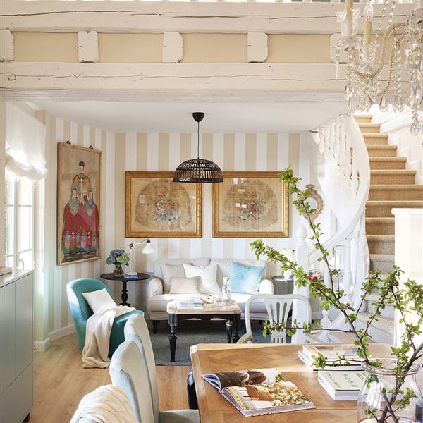 Sofá junto al comedor con papel pintado a rayas, escaleras, butaca azul y escaleras que conectan con el segundo piso y el altillo