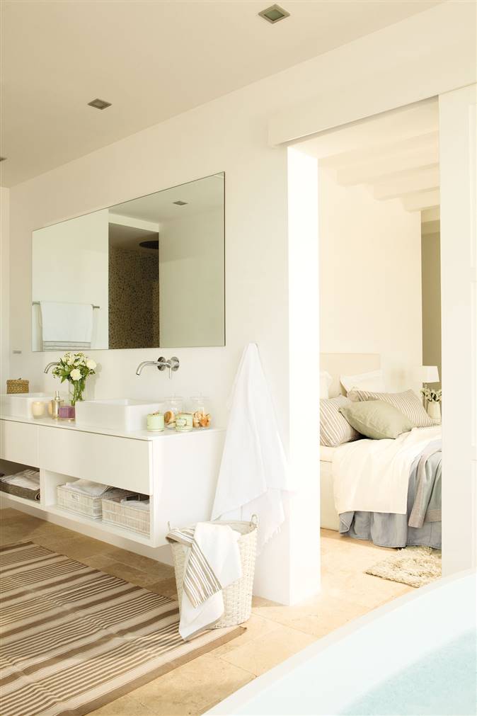 Un baño abierto al dormitorio con un lavamanos doble y un mueble volado en blanco