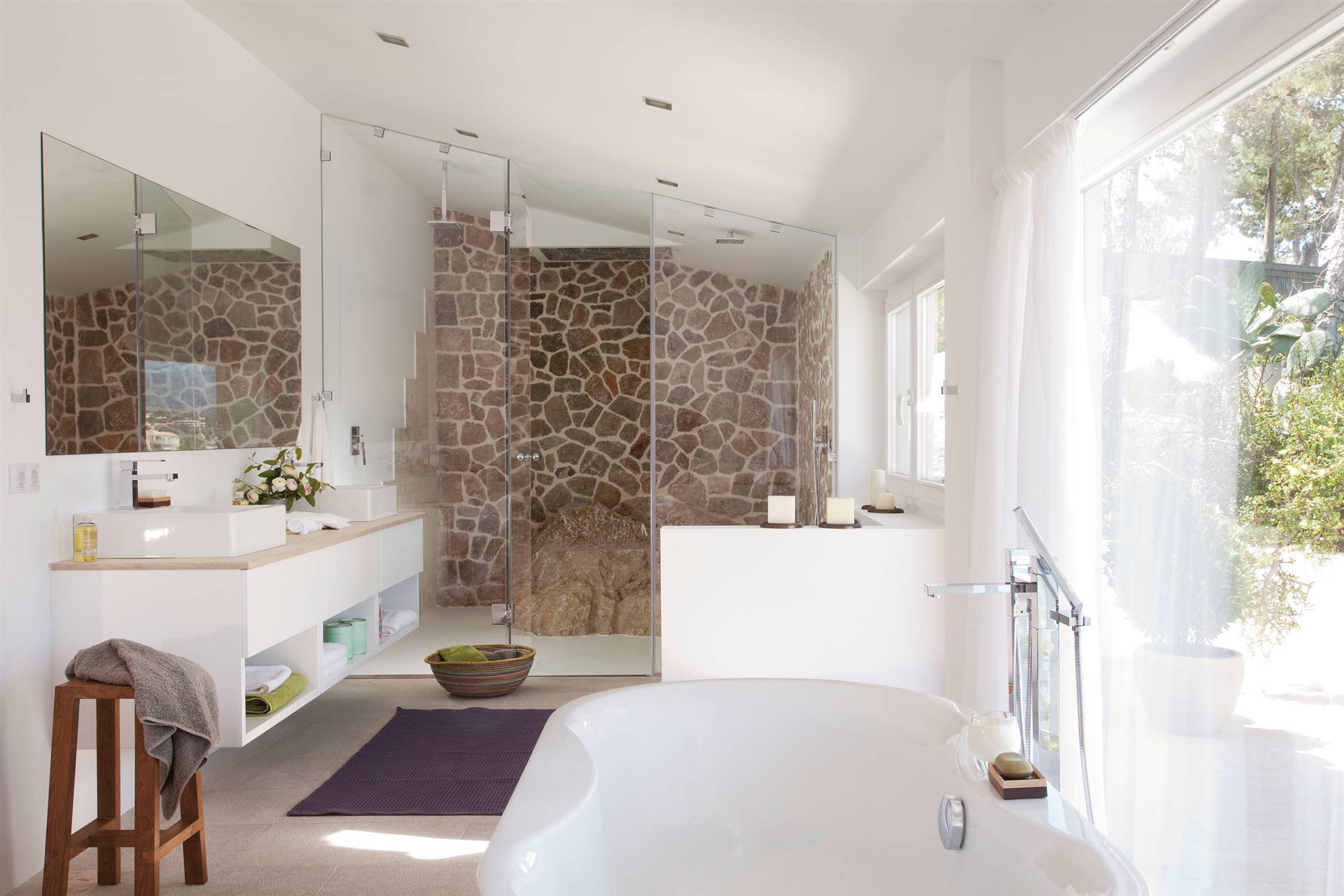 Baño grande de estilo moderno con pared de piedra en la ducha y bañera exenta.