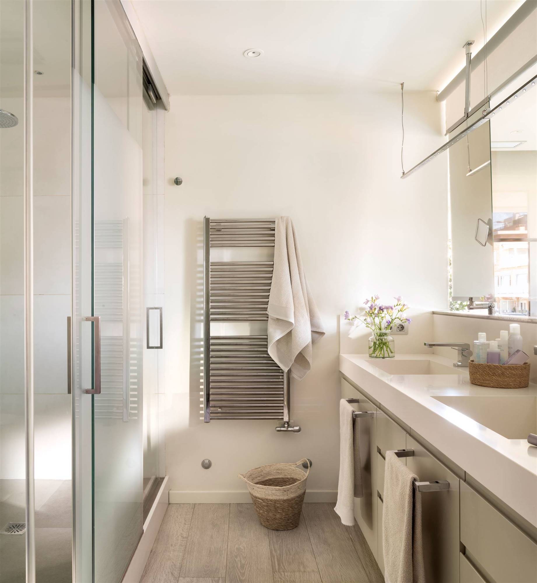 Baño con mueble a uno de los lados, cabinas con la ducha y el inodoro y toallero radiador. 