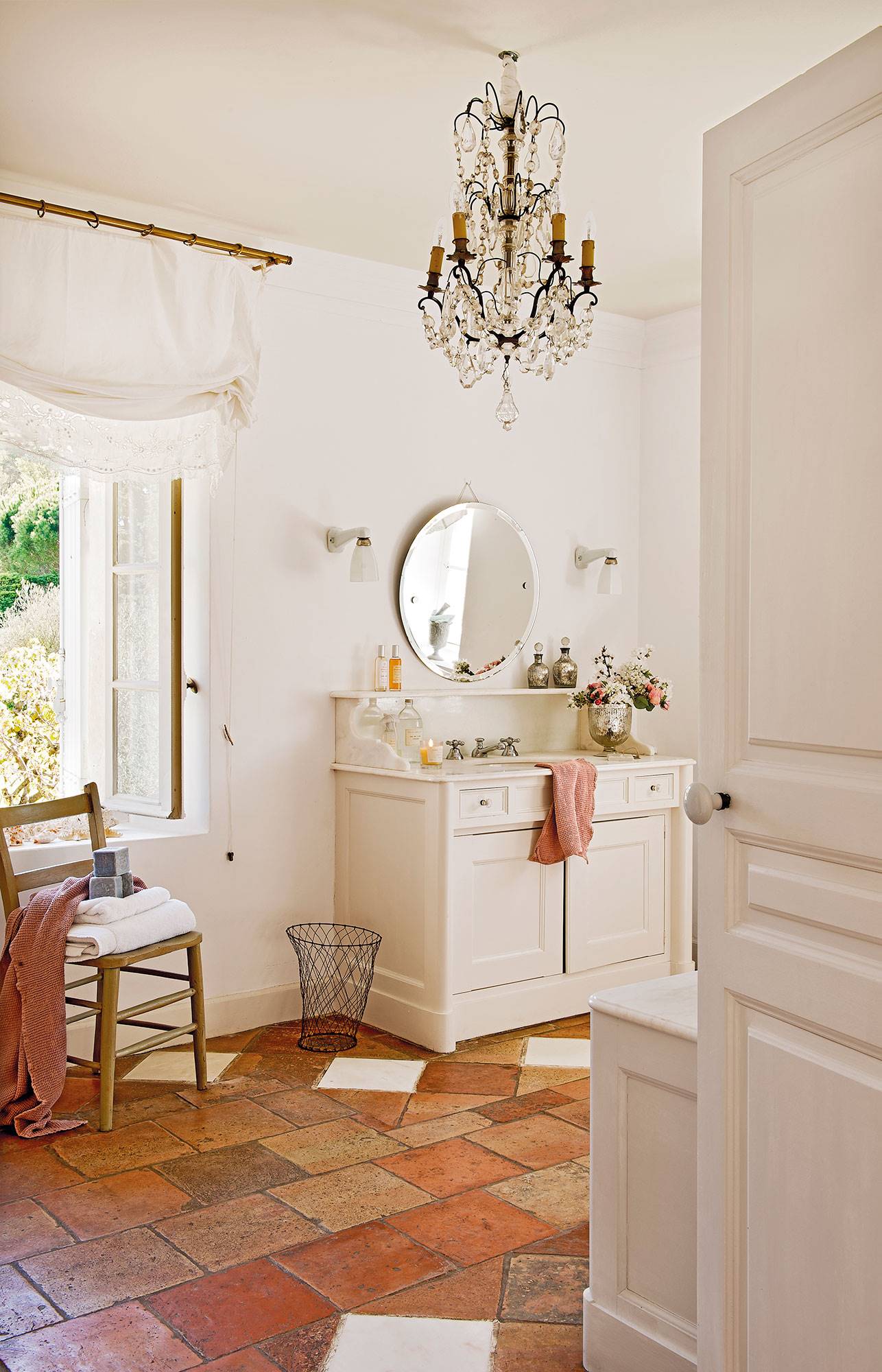 Baño con mueble de baño blanco, suelos de barro y lámpara de araña. 