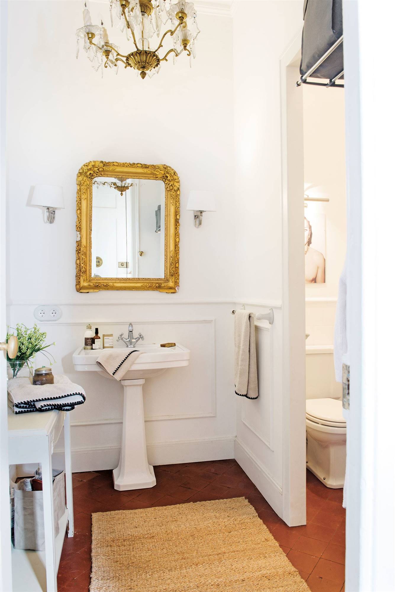 Baño con lavamanos de pedestal y espejo con marco dorado. 
