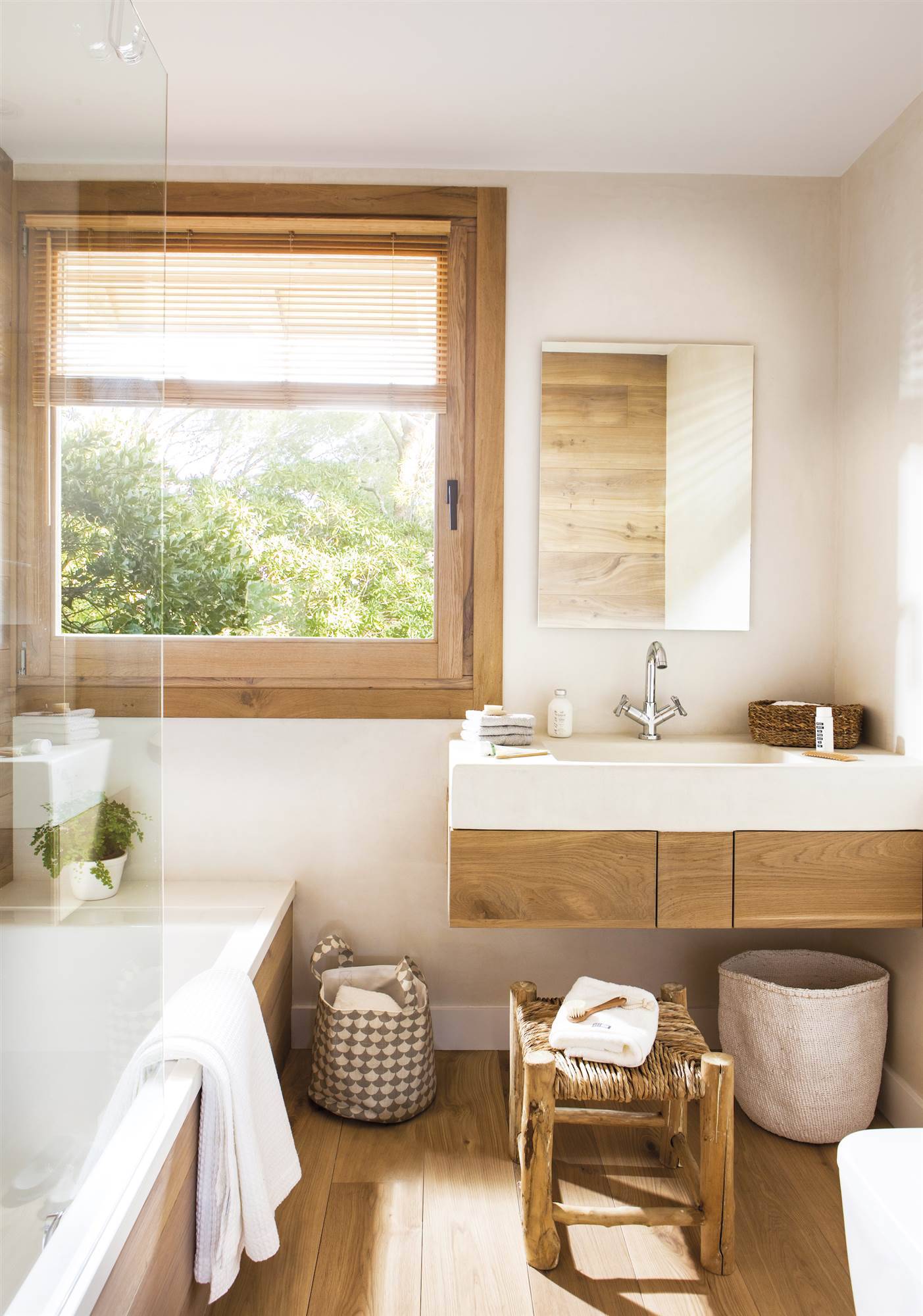 Baño en tonos blancos con suelo, mueble del lavamanos y detalles decorativos de madera. 