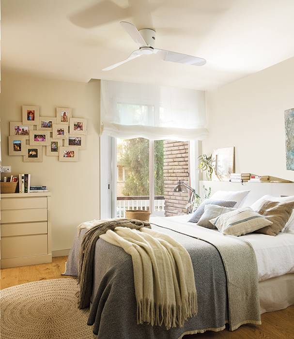 Dormitorio con cortina blanca, plaid, alfombra de fibras y composición de cuadros. 