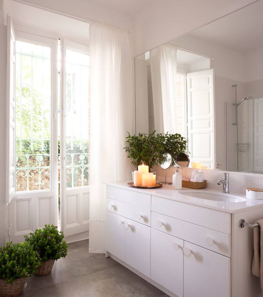 Baño con mueble de color blanco y espejo rectangular grande. 