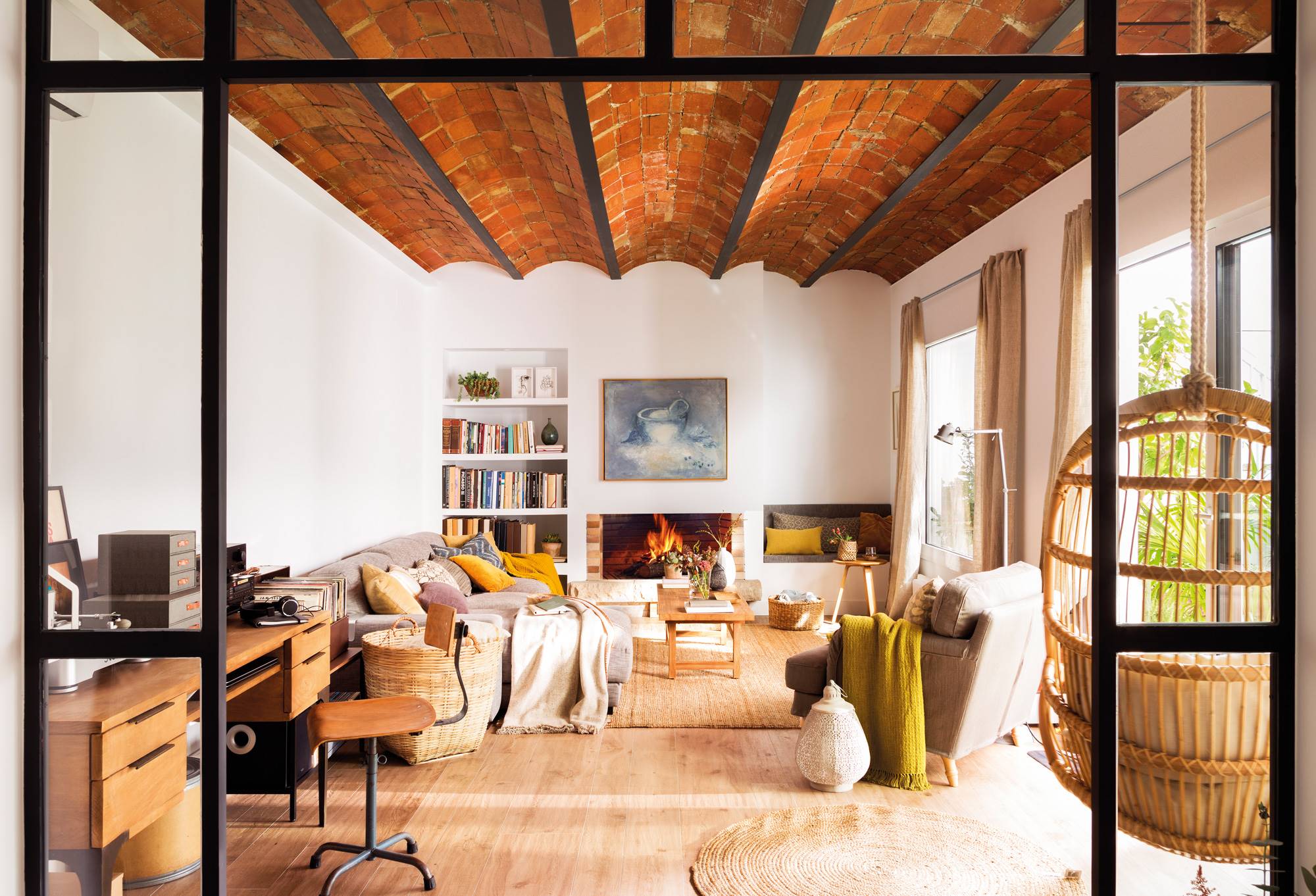 Salón con sofá gris, complementos de fibras naturales y techo de bóvedas y vigas.