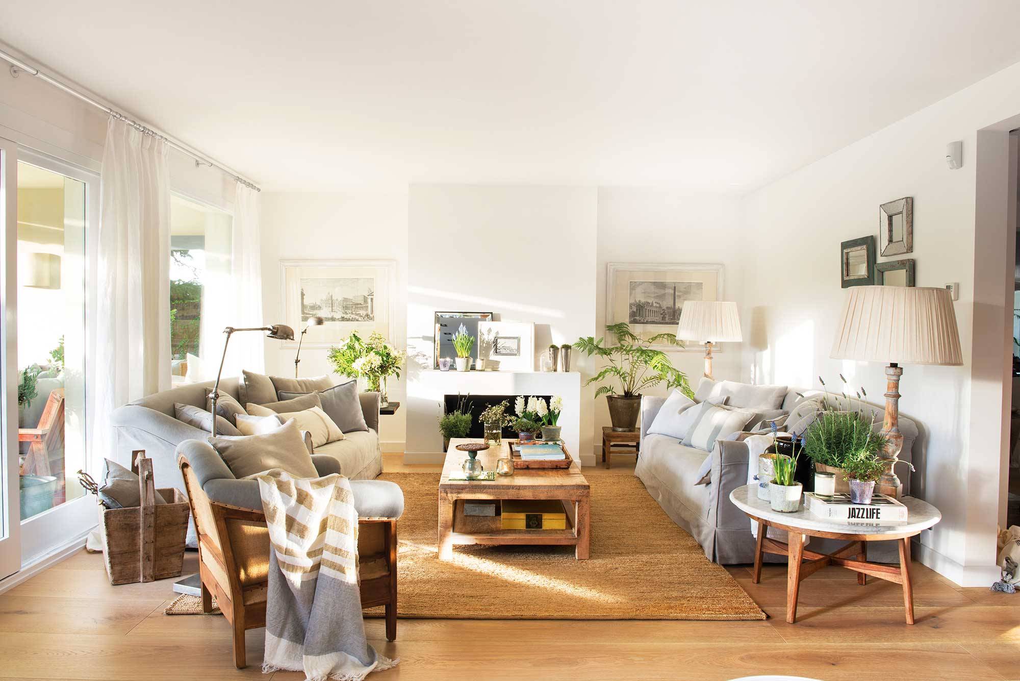 Salón con sofás grises, paredes blancas, accesorios de fibras naturales, chimenea y salida al jardín.