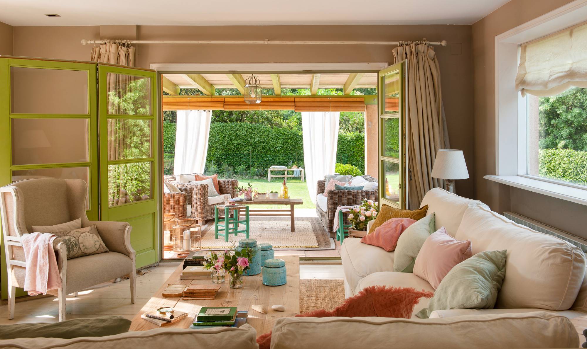Salón con sofás beige y cojines rosas y azules abierto al porche. 